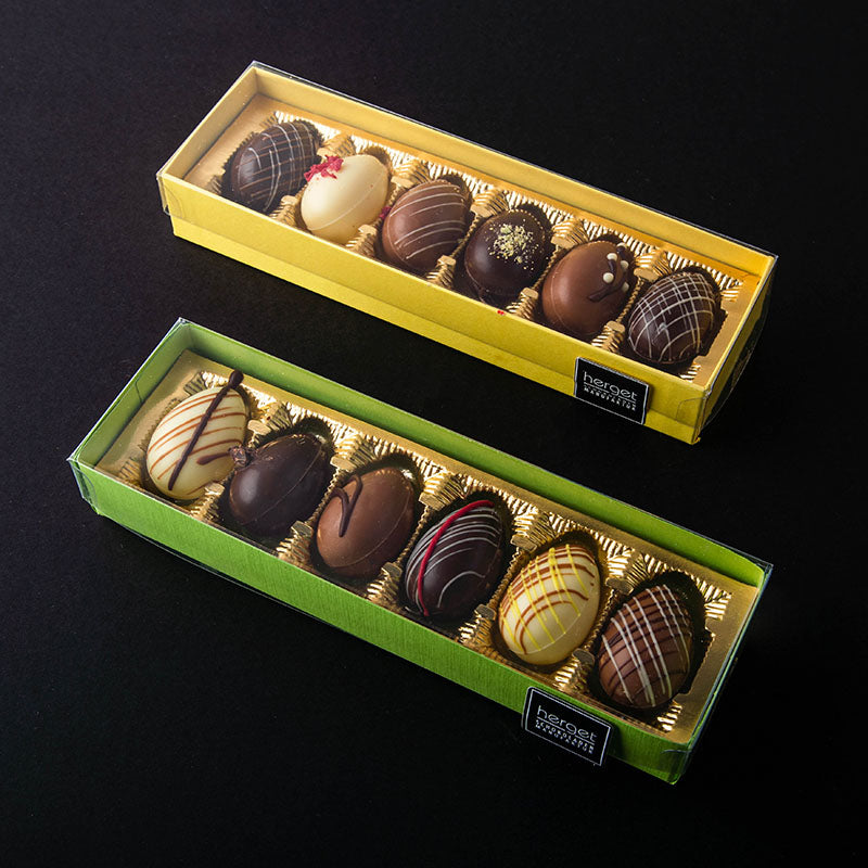 zwei 6er Stangen gefüllter Schokoladeneier in gelber und grüner Verpackung mit transparentem Deckel