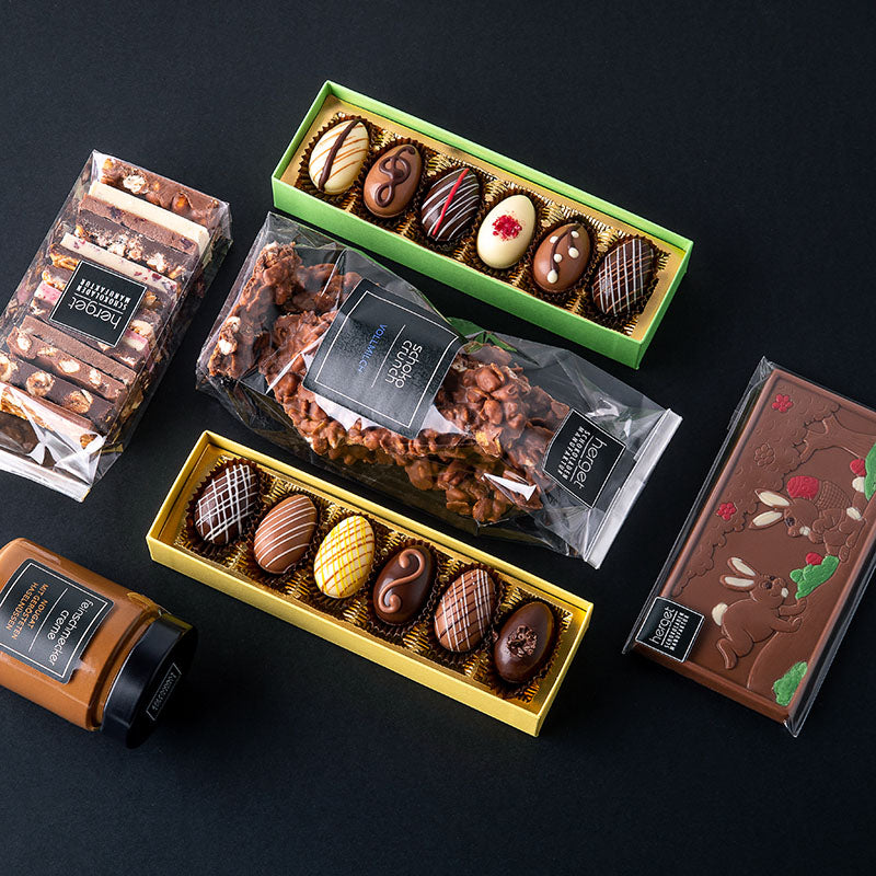 verschiedene Schokoladenprodukte zu Ostern auf dunklem Hintergrund u.a. Crunch, eine bemalte Schokoladentafel, gefüllte Schokoladeneier, Feinschmeckerschokolade und Feinschmeckercreme